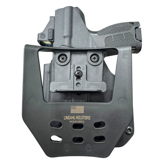 A black tactical holster with a mounted quick-release clip and a handgun partially inserted, photographed on a plain white background. The holster is branded with 'LINDAHL HOLSTERS' and 'MADE IN AMERICA' printed on the front.