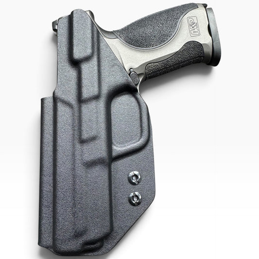 A black textured Kydex holster containing a semi-automatic handgun, shown from a top-down angle on a light gray background. The holster features molded contours and two visible silver screws, and the handgun has a textured black grip and a silver metallic frame.