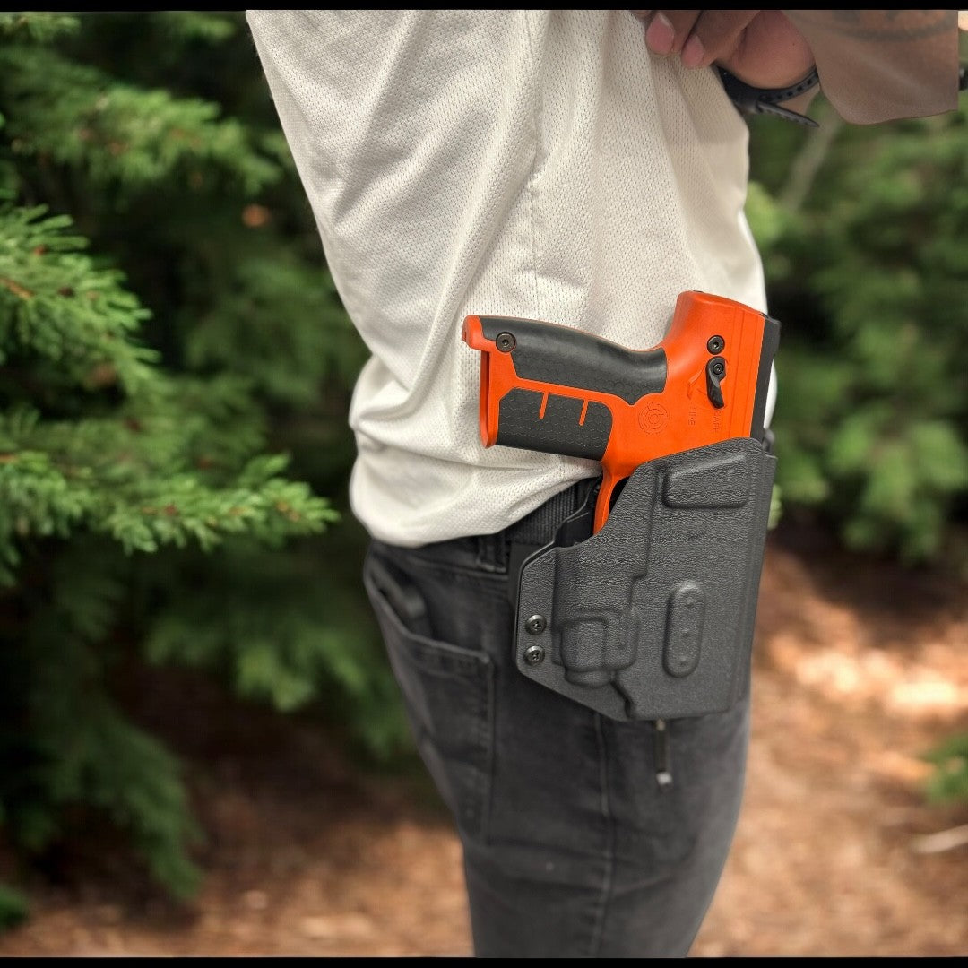 Orange and black gun in a holster on a person's waist with a blurred green background