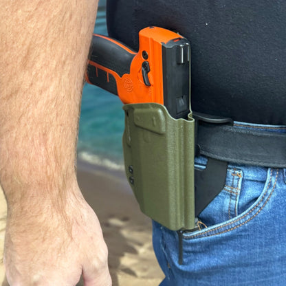 Orange and black gun in a green holster on a person's waistband with a blurred background.